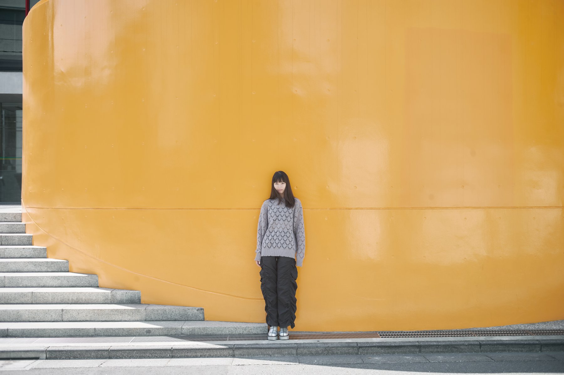 黄色い壁の前に立つ人物のポートレート 撮影：長田慶